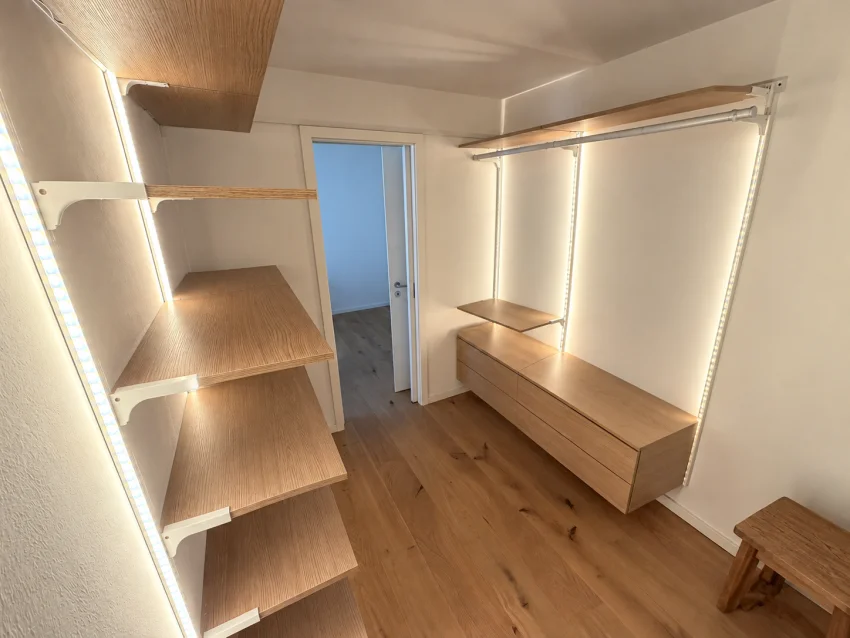 Leeres Ankleidezimmer mit Holzregalen, Kleiderstangen, Schubladen und Beleuchtung