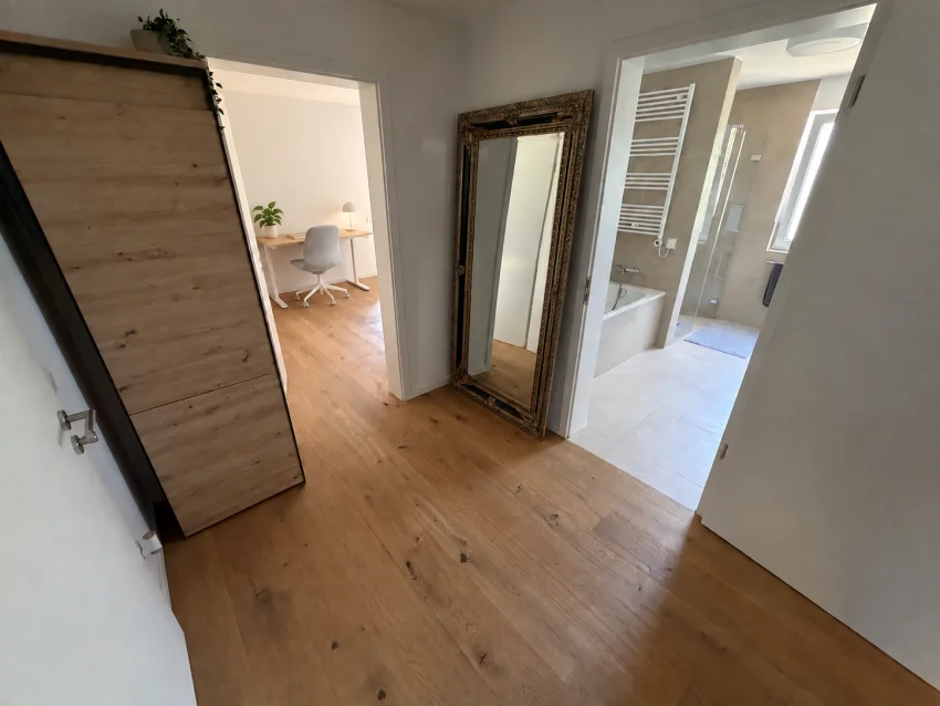 Flur mit Garderobe und Spiegel, Blick zum Schreibtisch mit hellgrauem Stuhl und ins Tageslichtbad