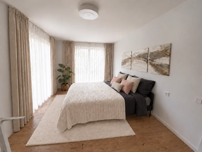 Helles Schlafzimmer mit cremefarbenen Textilien und Vorhängen vor zwei Fenstertüren