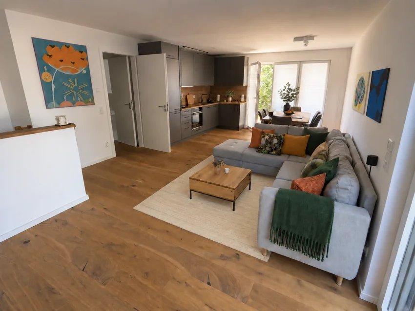 Wohnbereich mit offener Küche, Sofa und Essplatz am Fenster